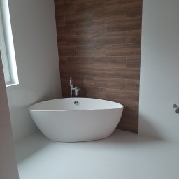 A.F. KOMFORT ADAM FIGURSKI - Nowoczesna łazienka z wolnostojącą wanną na białej podłodze. Ściana wyłożona płytkami imitującymi drewno. Minimalistyczna armatura i jasne wnętrze.