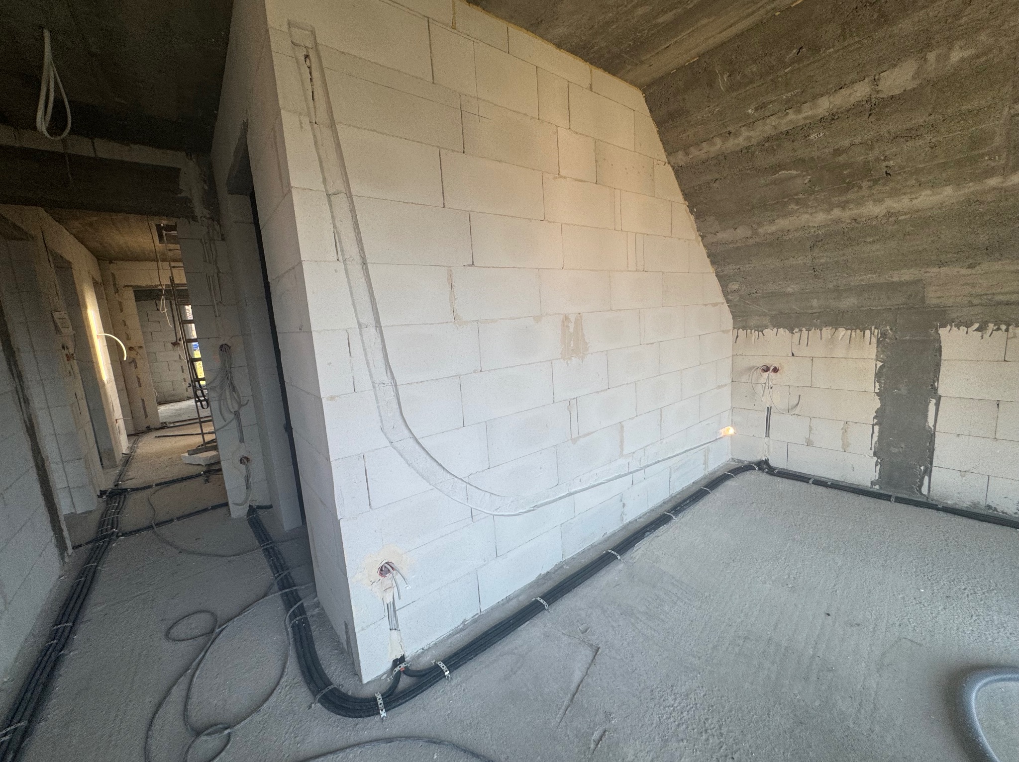 Surowy stan: instalacja przewodów wentylacyjnych i elektrycznych w budynku z betonu komórkowego przed wykończeniem. Widoczne kable i rury prowadzone po ścianach i podłodze.