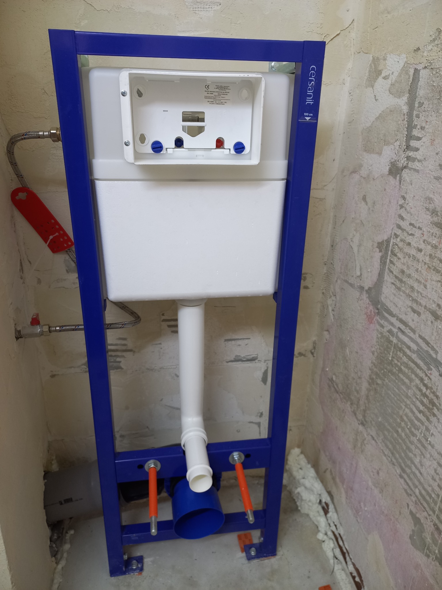 Stelaż podtynkowy Cersanit w trakcie montażu, widoczne przyłącza wody i kanalizacji. Ściany w surowym stanie, przygotowane do dalszych prac wykończeniowych.