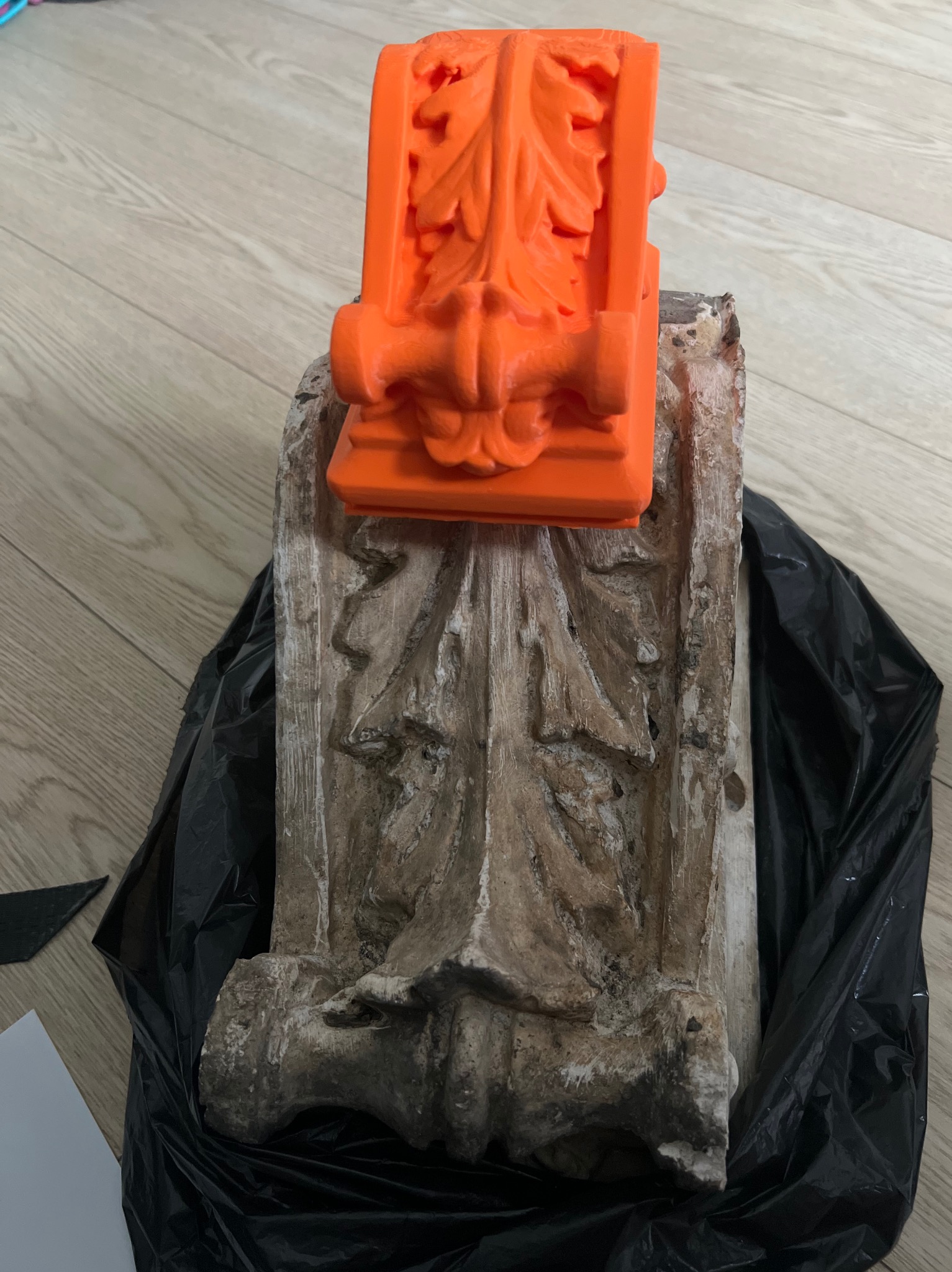 Pomarańczowy, precyzyjny model dekoracyjny z tworzywa sztucznego, umieszczony na odrestaurowanym, zabytkowym elemencie architektonicznym z ornamentami.