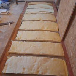 Lagrance - Izolacja podłogi z wełny mineralnej w trakcie prac wykończeniowych. Widoczne fragmenty konstrukcji podłogi i ściany z płyty OSB. Ujęcie z góry, w trakcie realizacji.