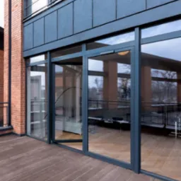 Loftowy balkon z dużymi, grafitowymi drzwiami przesuwnymi i drewnianą podłogą. Widok na zewnątrz odbija się w szybach.