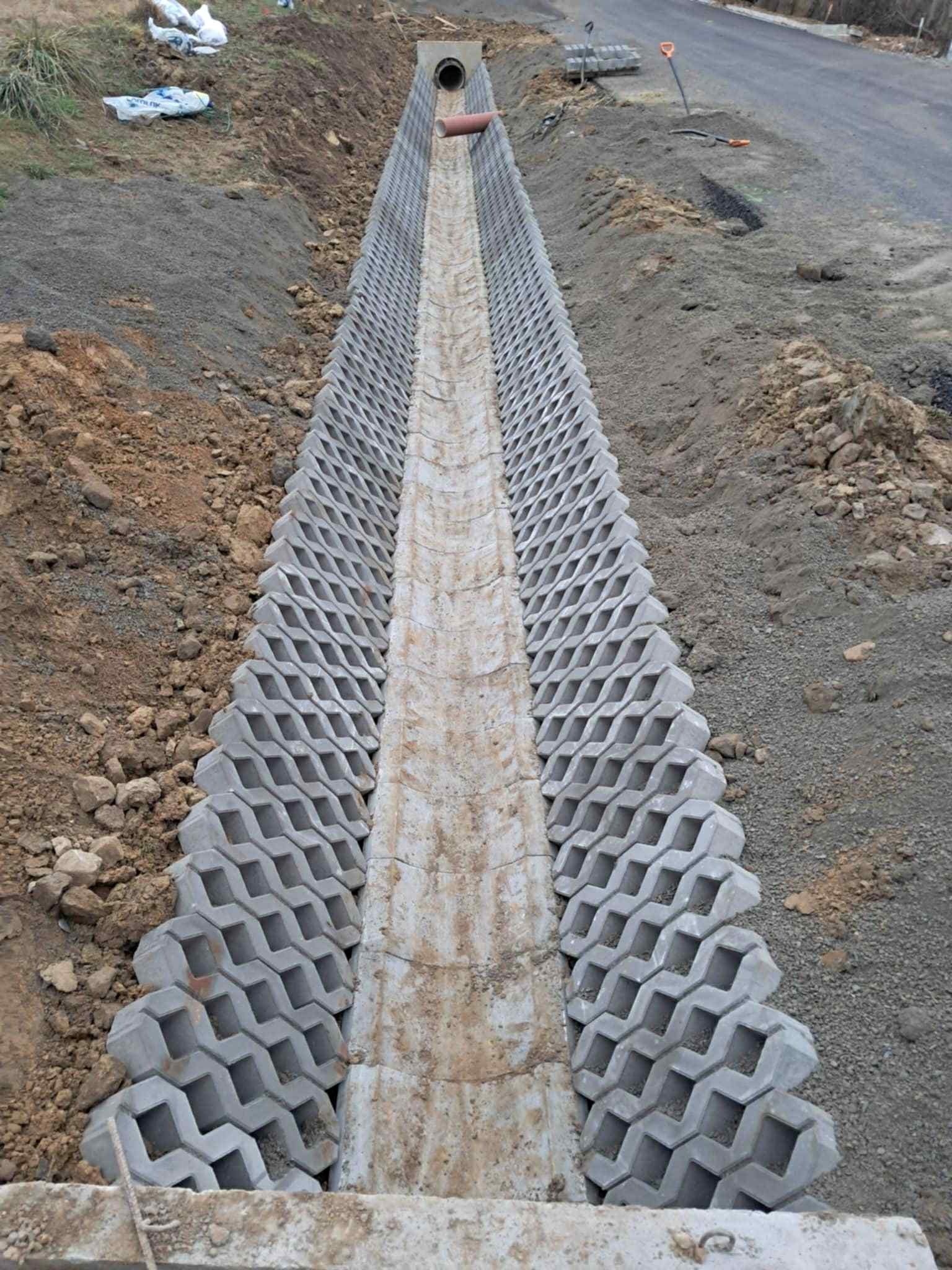 Ukończony drenaż liniowy z ażurowych betonowych elementów, widok z góry, teren po bokach wyrównany, droga w tle.