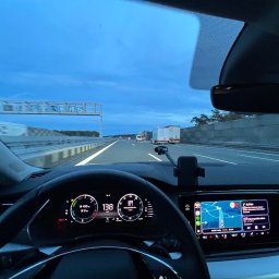 Pago Houses - Wnętrze samochodu w trakcie jazdy autostradą, widok z perspektywy kierowcy na deskę rozdzielczą z nawigacją i prędkościomierzem wskazującym 138 km/h, w tle inne pojazdy.