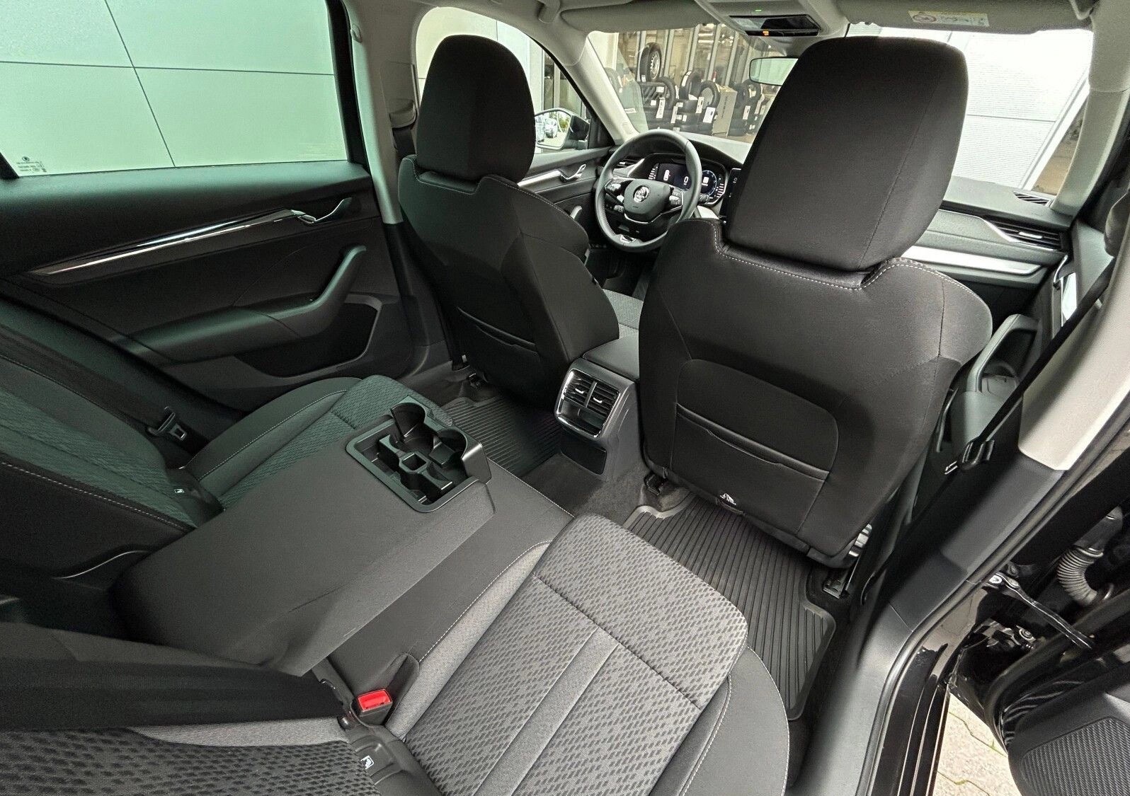 Wnętrze czarnego samochodu osobowego z widocznymi tylnymi siedzeniami, podłokietnikiem z uchwytami na napoje i zagłówkami. Widoczna deska rozdzielcza i kierownica.