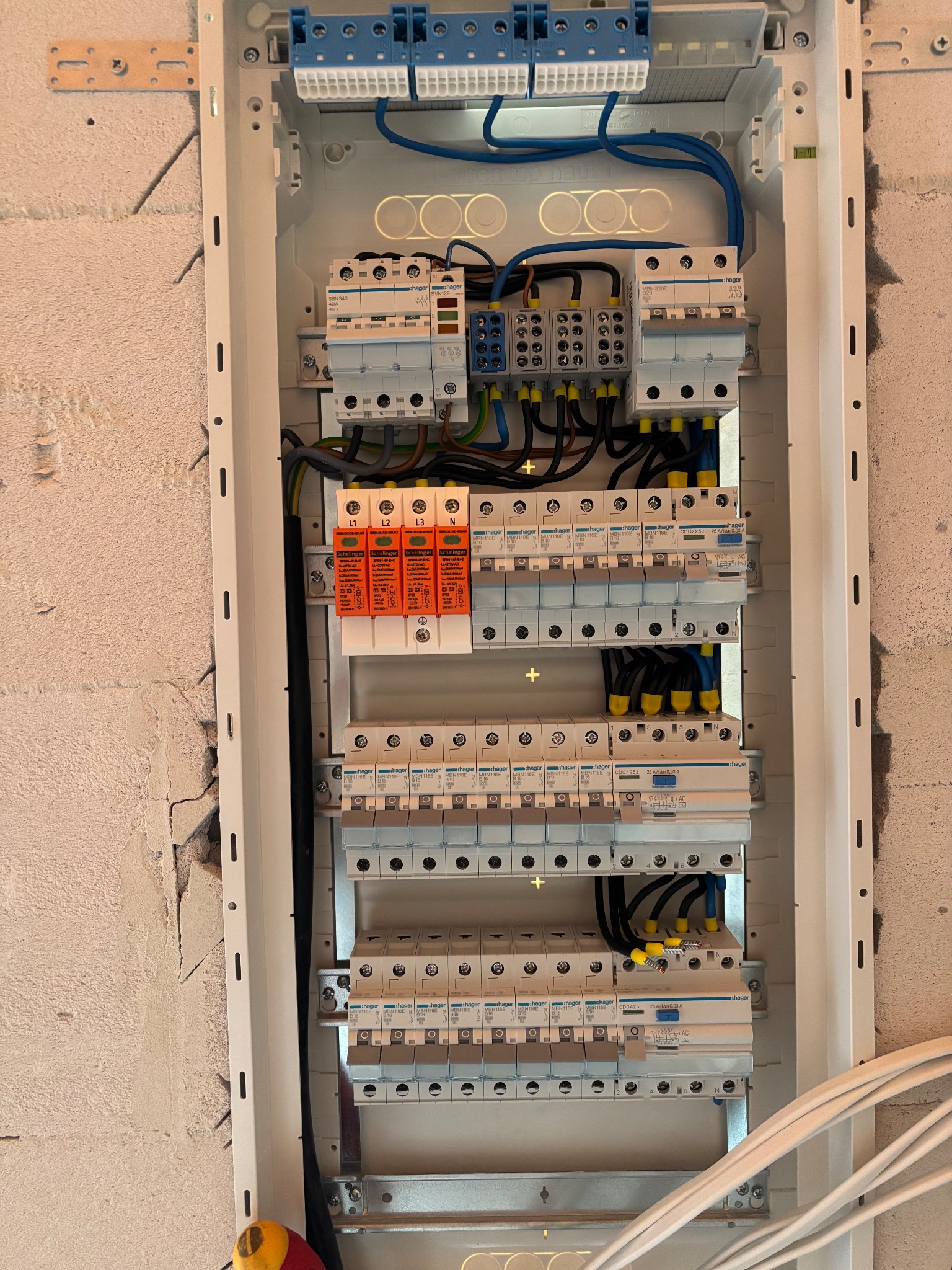 Rozdzielnica elektryczna Hager z zabezpieczeniami, widoczne przewody i aparatura modułowa, zamontowana na surowej ścianie. Detal instalacji elektrycznej w budynku.
