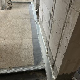 VoltBit - Montaż metalowych profili przy ścianie z betonu komórkowego, uszczelnionych pianką montażową. Widoczne elementy instalacji w surowym stanie.