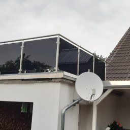 Natis Paweł Stankiewicz - Szklana zabudowa balkonu z metalową ramą w Gubinie. Nowoczesny design, ciemne szkło, widok z dołu na balkon z anteną satelitarną i fragmentem dachu.