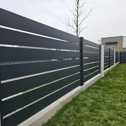 Natis Paweł Stankiewicz - Nowoczesne ogrodzenie panelowe w kolorze grafitowym z betonową podmurówką i słupkami, na tle zielonego trawnika i domu. Minimalistyczny design.
