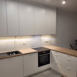 Interier - Nowoczesna kuchnia z białymi frontami, drewnianym blatem i marmurowym panelem. Oświetlenie LED podkreśla detale. Widoczny piekarnik Bosch i zlewozmywak.