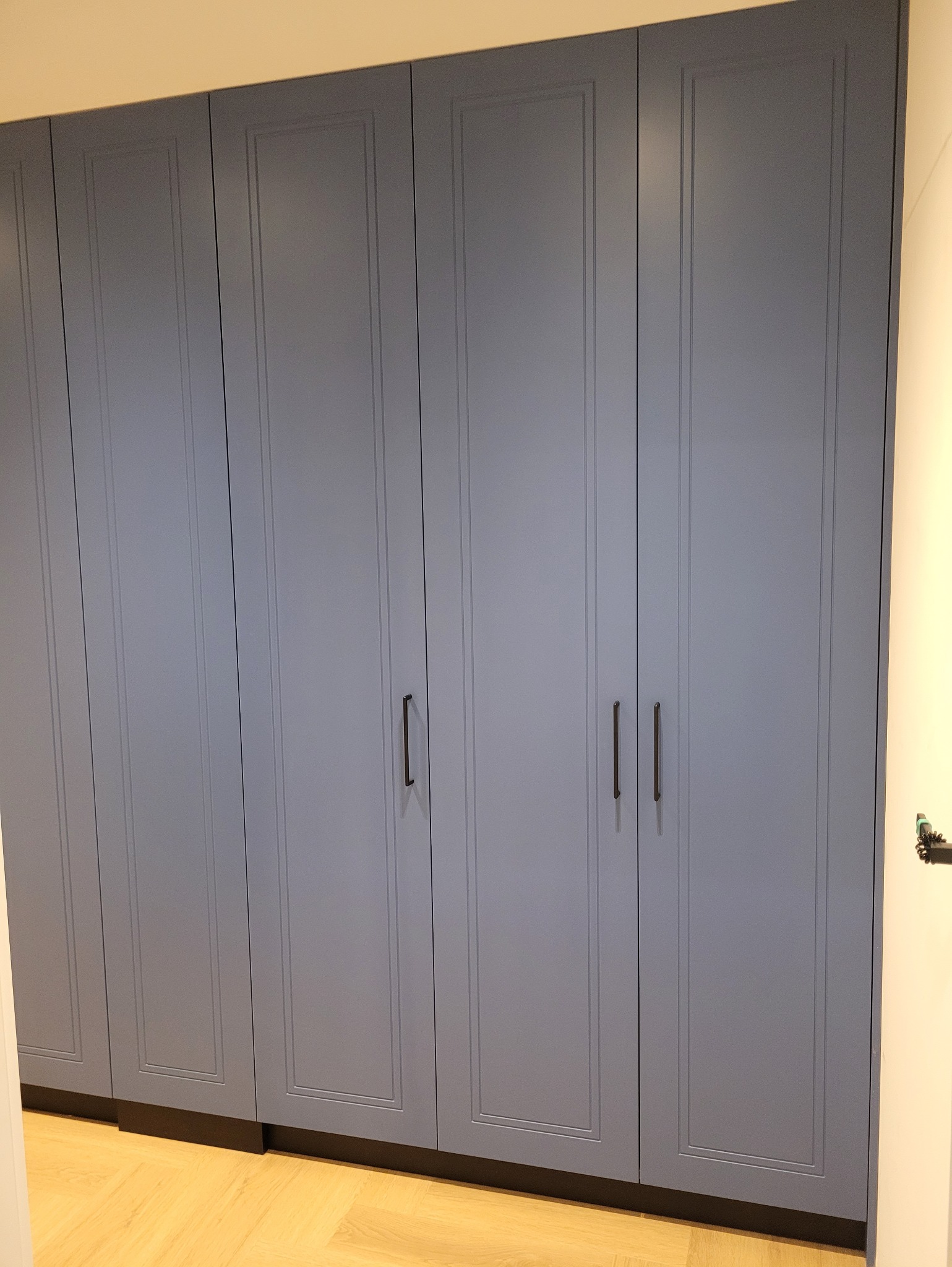 Szara szafa wnękowa z frezowanymi frontami i minimalistycznymi uchwytami, widoczna na tle jasnej podłogi i ściany. Klasyczny design z nowoczesnym akcentem.