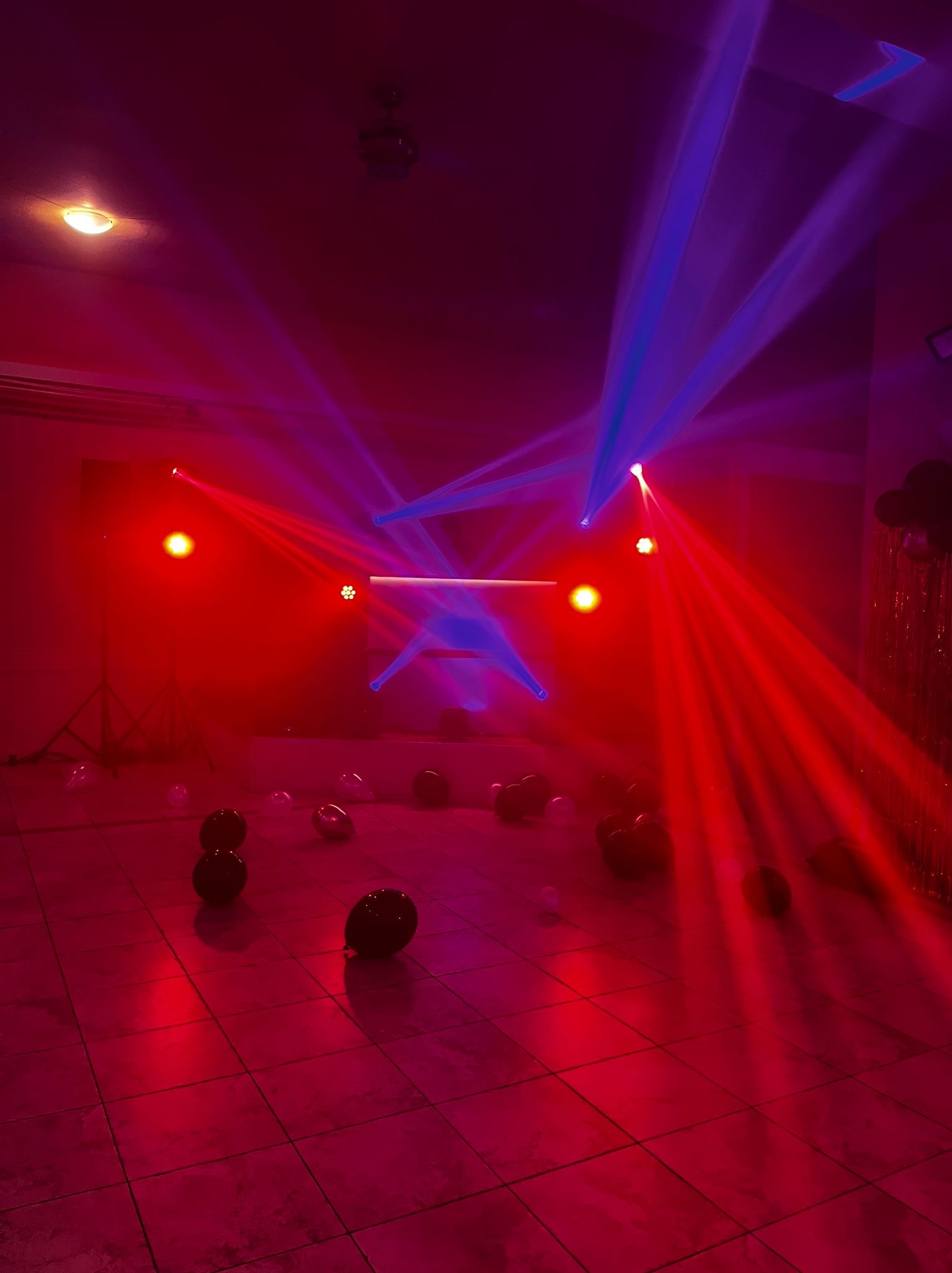 Oświetlenie sceniczne w czerwieni i błękicie, z czarnymi balonami na podłodze z płytek. Efektowne światła tworzą atmosferę imprezy.