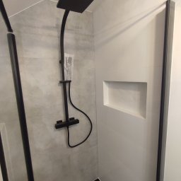 DUŻY MAŁY REMONT Damian Łoniewski - Nowoczesna kabina prysznicowa z czarną armaturą i wnęką w ścianie wyłożonej białymi płytkami. Szare płytki na ścianie z deszczownicą. Minimalistyczny design.