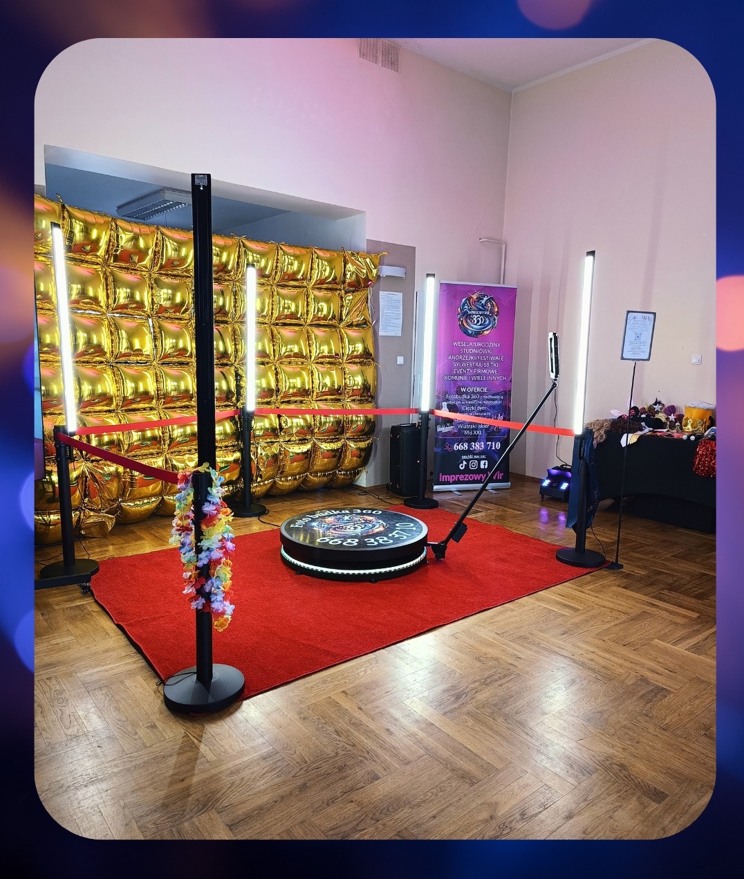 Fotobudka 360 na czerwonym dywanie z dekoracją z balonów i oświetleniem. Widoczny plakat z ofertą i rekwizyty. Parkiet w jodełkę.