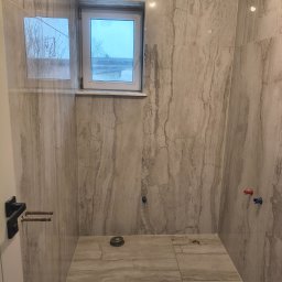 Mykhailo Hnatiuk - Wykończona łazienka z marmurowymi płytkami, widoczne okno i przygotowane instalacje. Minimalistyczny design z elementami w kolorze szarym i białym.