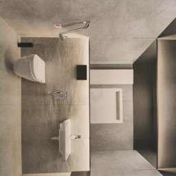 Mykhailo Hnatiuk - Minimalistyczna łazienka z szarymi płytkami, widziana z góry. Umywalka, toaleta i kabina prysznicowa w nowoczesnym stylu. Oświetlenie punktowe i geometryczne detale.