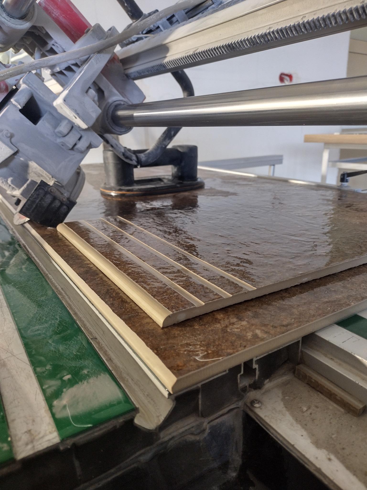 Cięcie brązowej płytki ceramicznej z rowkami na mokro za pomocą profesjonalnej przecinarki do glazury. Widoczne narzędzie i fragment płytki.