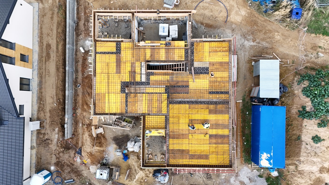 Z lotu ptaka: Żółte szalunki i zbrojenia fundamentów domu jednorodzinnego w Lublinie. Widoczne elementy konstrukcyjne i teren budowy.
