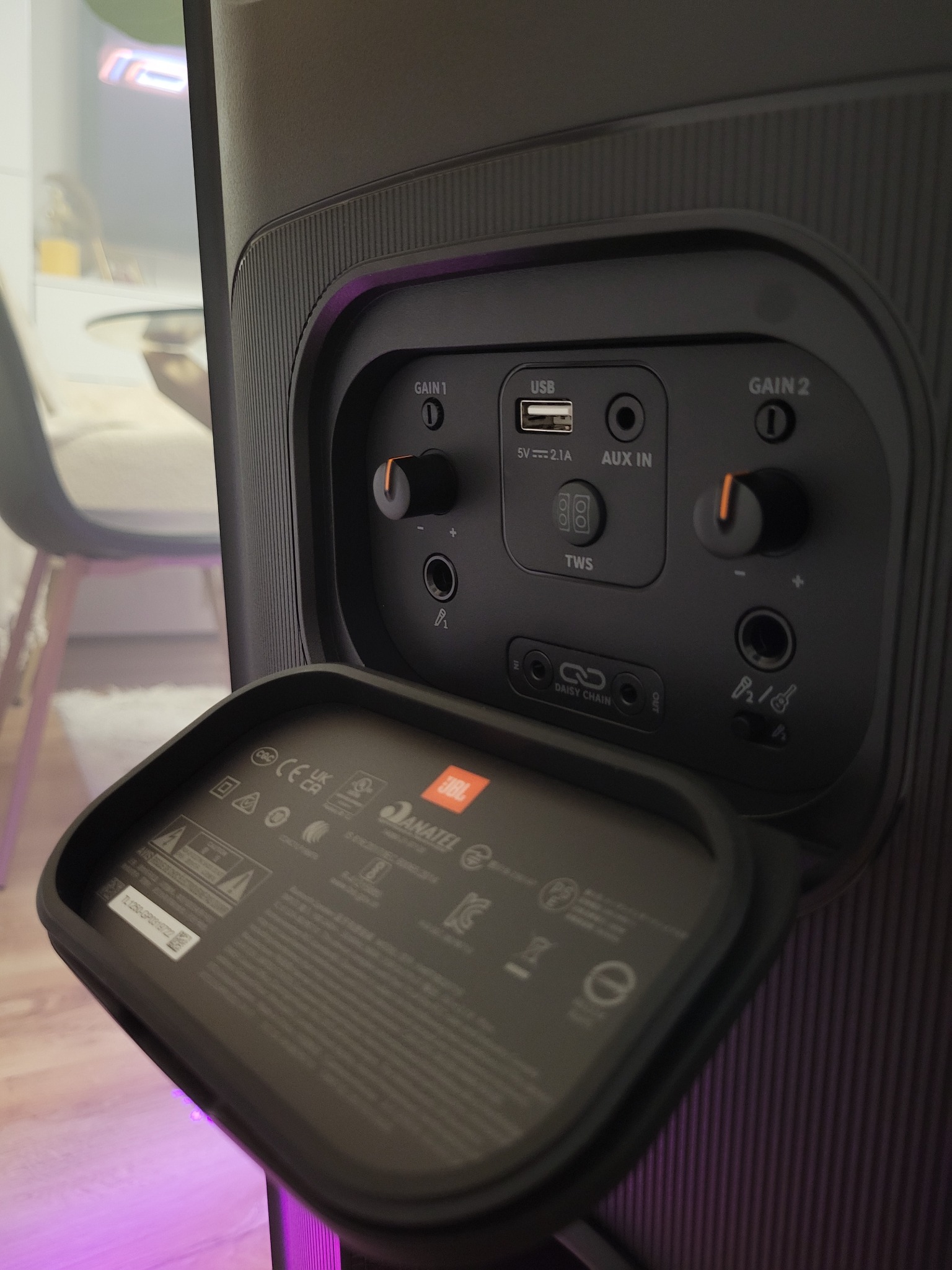 Panel tylny głośnika JBL Partybox z otwartą klapką, widoczne porty USB, AUX, wejścia mikrofonowe i regulacja wzmocnienia. Detale obudowy i oznaczenia certyfikacyjne.