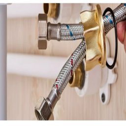 INSTALATOR S.C. KAZIMIERZ OZIMEK WOJCIECH OZIMEK - Podłączenie elastycznego węża do instalacji wodnej. Widoczna dłoń montera, elementy złączek i rur. Ujęcie z bliska, ukazujące detale połączenia.