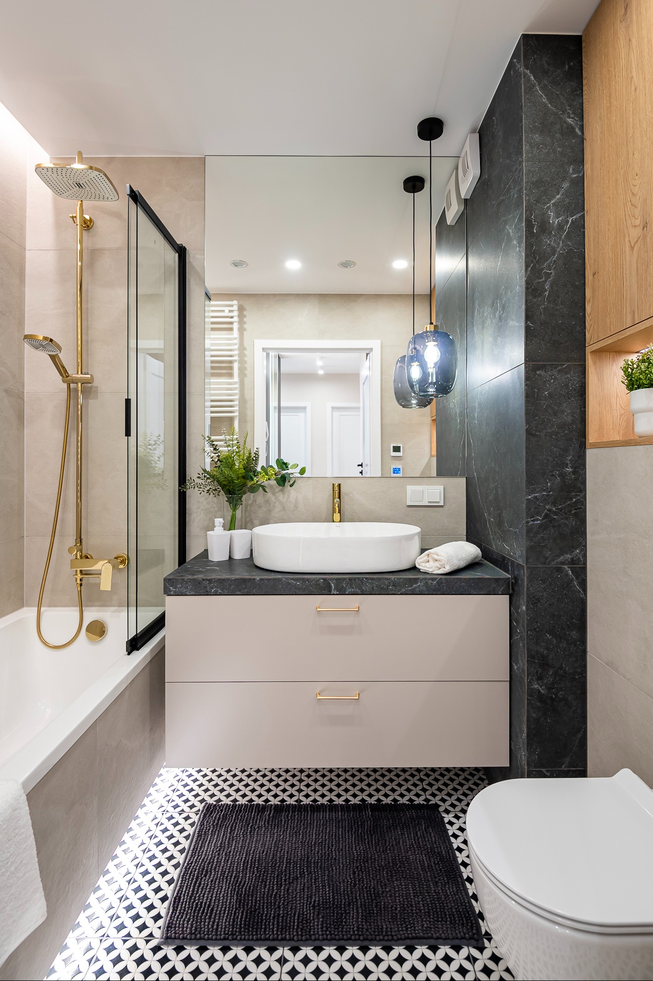 Nowoczesna łazienka z wanną, kabiną prysznicową, umywalką nablatową i czarno-białą podłogą. Złote akcenty armatury i oświetlenia dodają elegancji.