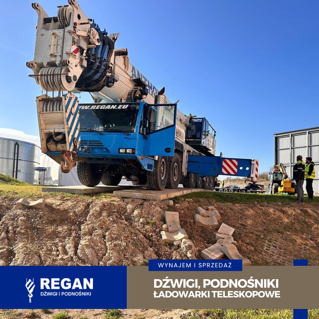 Niebieski dźwig samojezdny MAN na placu budowy, z wysuniętym ramieniem i otwartymi drzwiami kabiny, w tle zbiorniki i budynek. Wynajem i sprzedaż dźwigów.