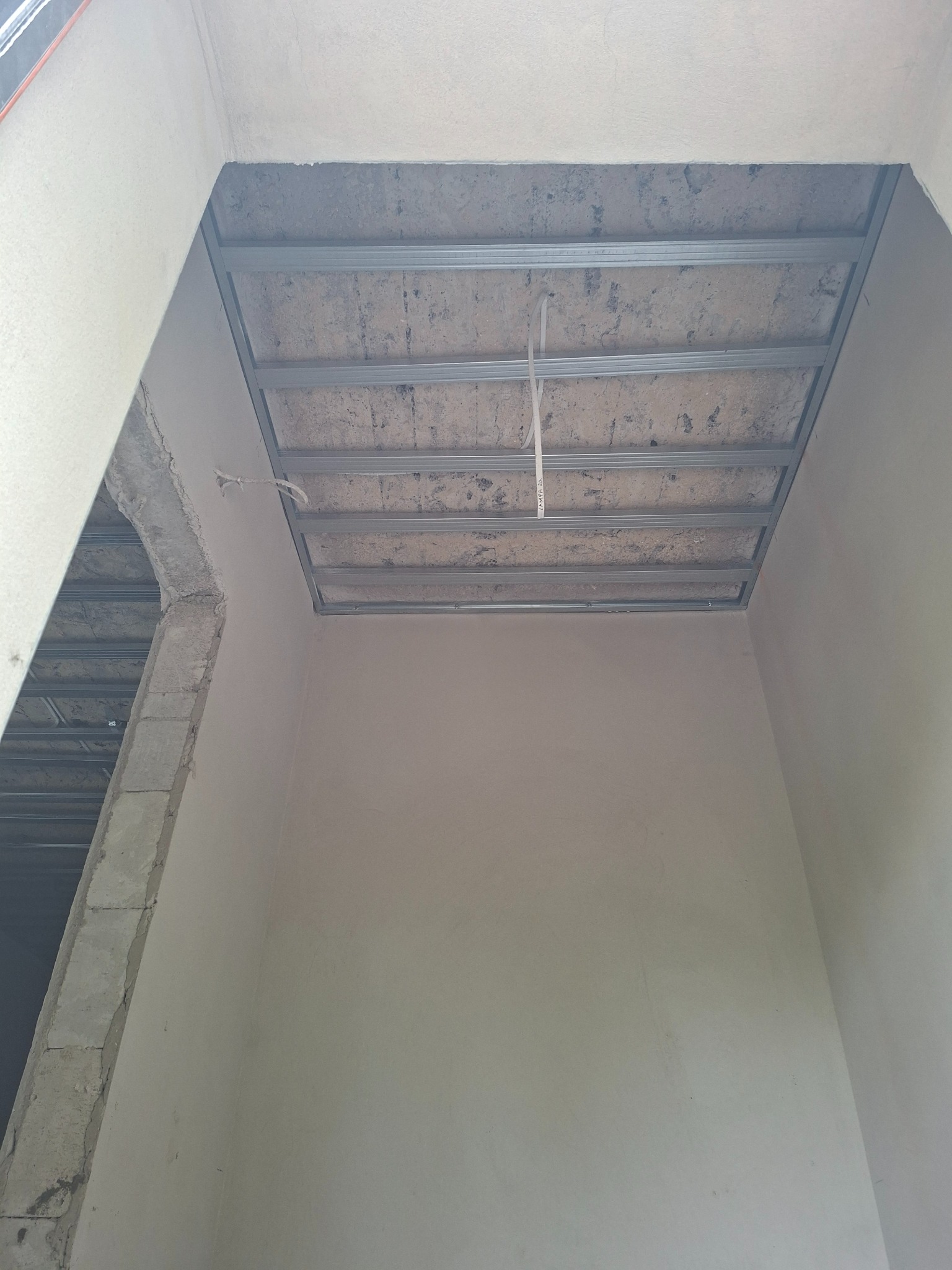 Montaż metalowej konstrukcji sufitu podwieszanego w surowym wnętrzu. Widoczne profile i fragment instalacji elektrycznej. Ściany przygotowane do dalszych prac.