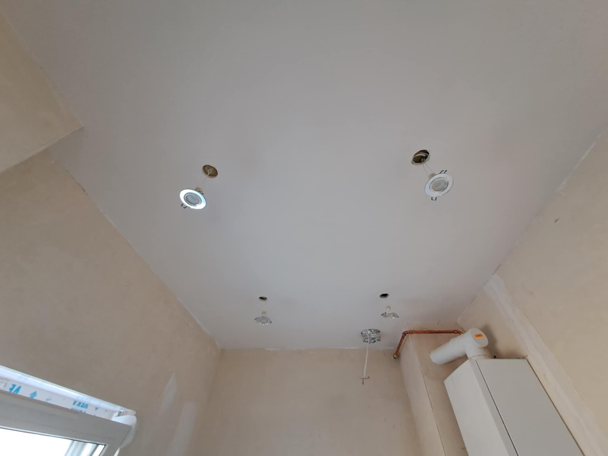 Biały sufit po szpachlowaniu z zamontowanymi punktami świetlnymi, widoczne ślady po instalacji. Ściany przygotowane do malowania. Ujęcie z dołu.