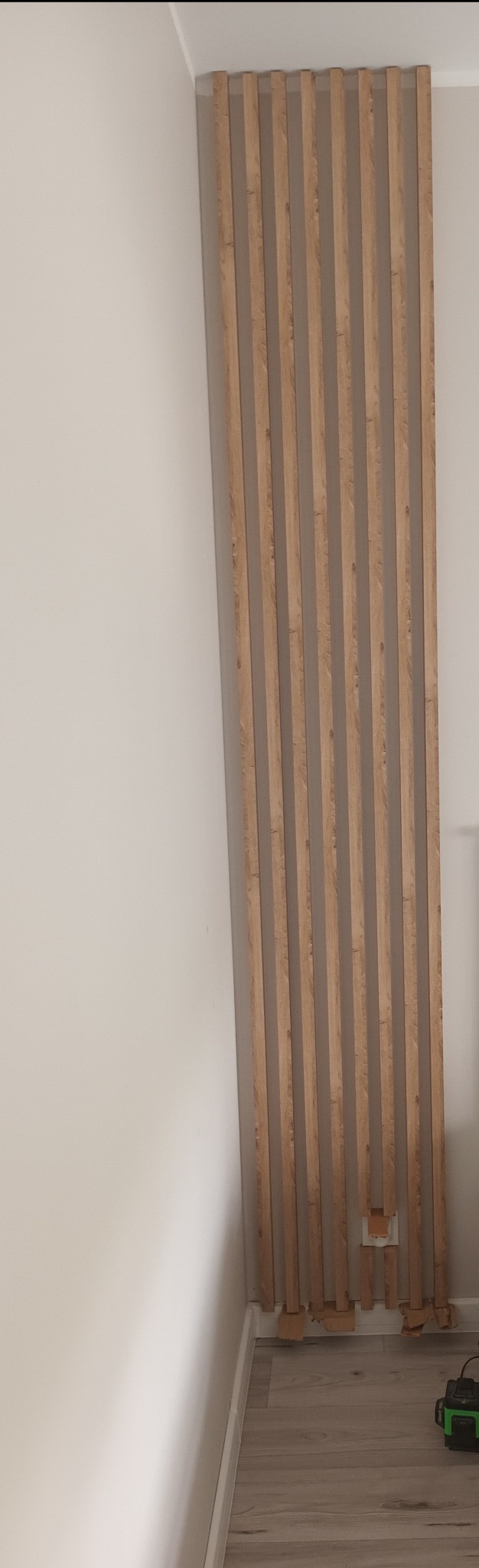 Montaż dekoracyjnych paneli ściennych z drewnopodobnym wzorem. Widoczne niedokończone prace przy podłodze i gniazdku elektrycznym. Jasne wnętrze.