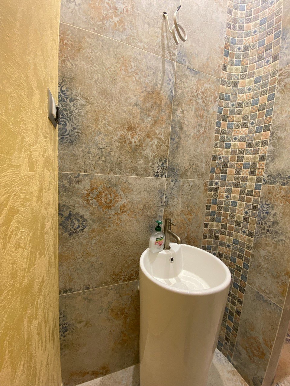 Umywalka kolumnowa i dekoracyjne płytki w łazience po remoncie w Kętrzynie. Widoczny fragment ściany z fakturą. Nietypowe wykończenie.