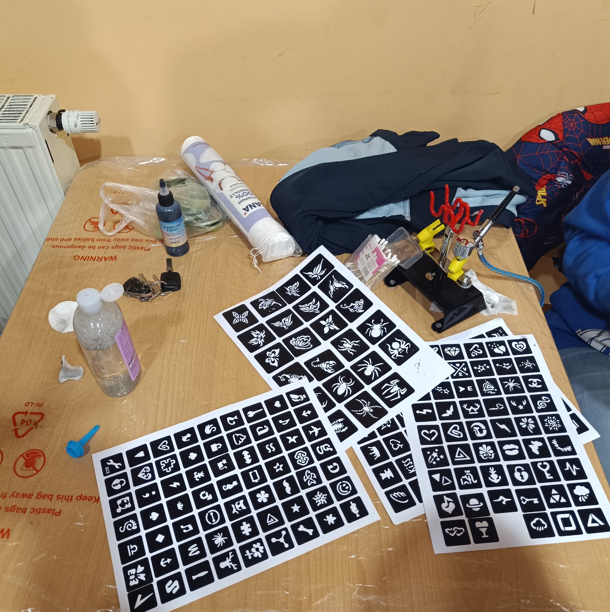 Stanowisko pracy z szablonami tatuaży, farbą do aerografu, wacikami i aerografem. Przygotowania do wykonania tatuażu tymczasowego.