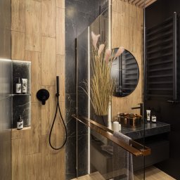 Usługi ogólnobudowlane Ad bud Adrian Kobędza - Nowoczesna łazienka z kabiną typu walk-in, drewnopodobnymi i marmurowymi płytkami, czarną armaturą i okrągłym lustrem. Minimalistyczny design z akcentami miedzi.