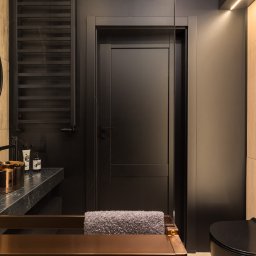 Usługi ogólnobudowlane Ad bud Adrian Kobędza - Nowoczesna łazienka w odcieniach czerni i drewna: miedziana umywalka, czarna armatura, drzwi i toaleta. Minimalistyczny design z akcentami naturalnego drewna.