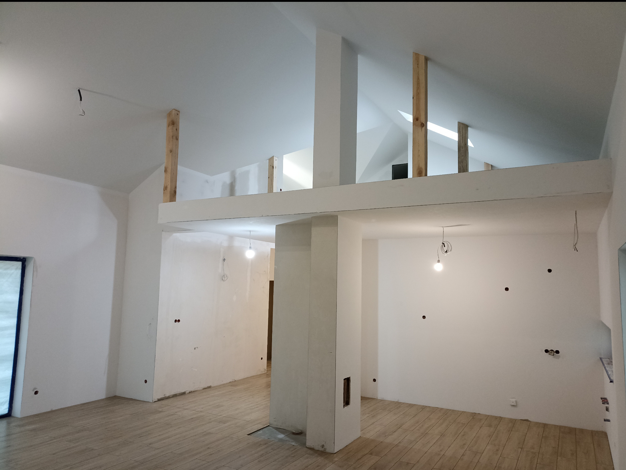 Wnętrze w trakcie prac wykończeniowych: drewniana podłoga, białe ściany z widocznymi punktami elektrycznymi, konstrukcja antresoli z drewnianymi belkami.