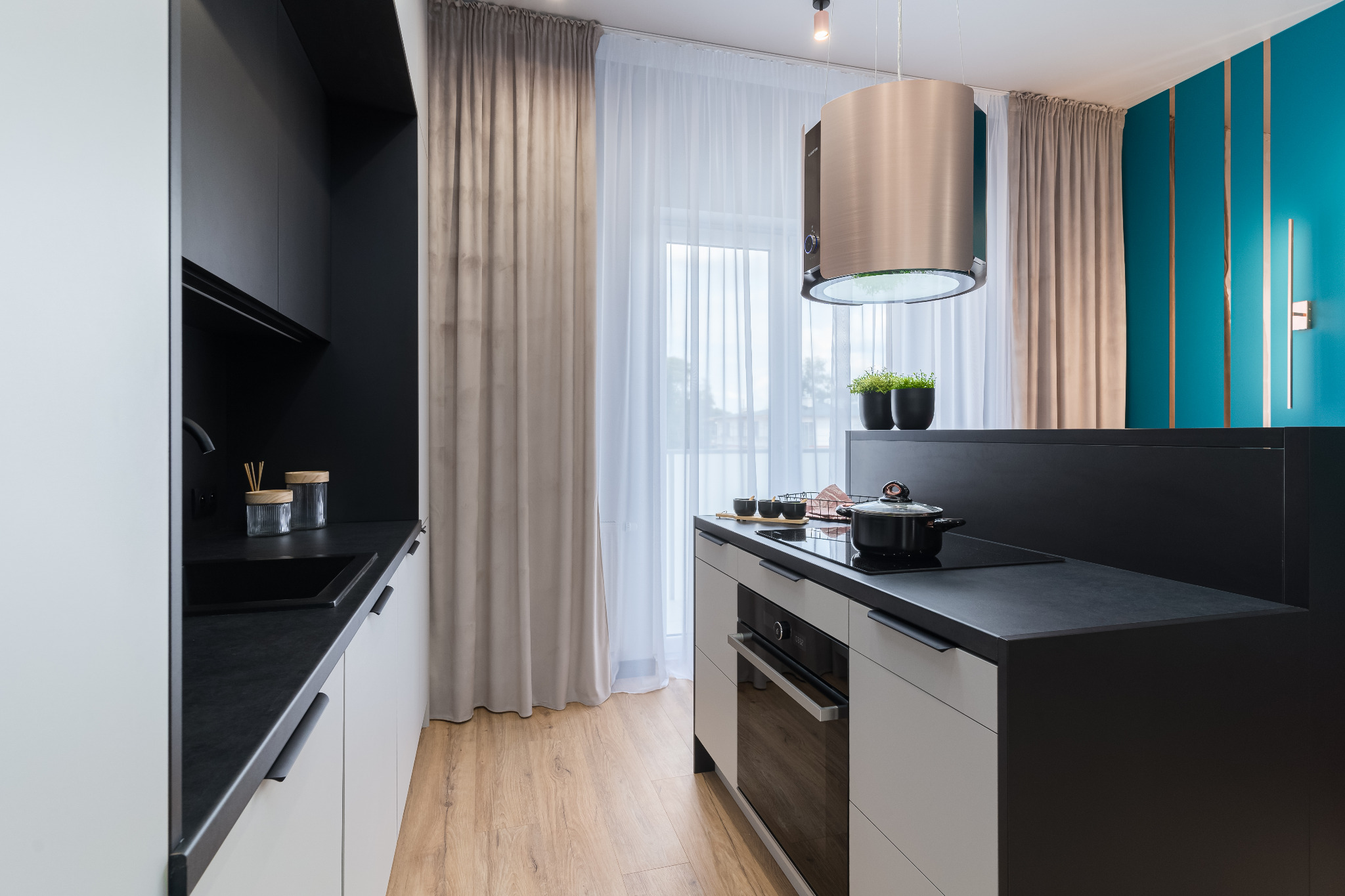 Nowoczesna kuchnia z czarnymi blatami i białymi szafkami, okap cylindryczny, turkusowa ściana z oświetleniem. Minimalistyczny design, drewniana podłoga.