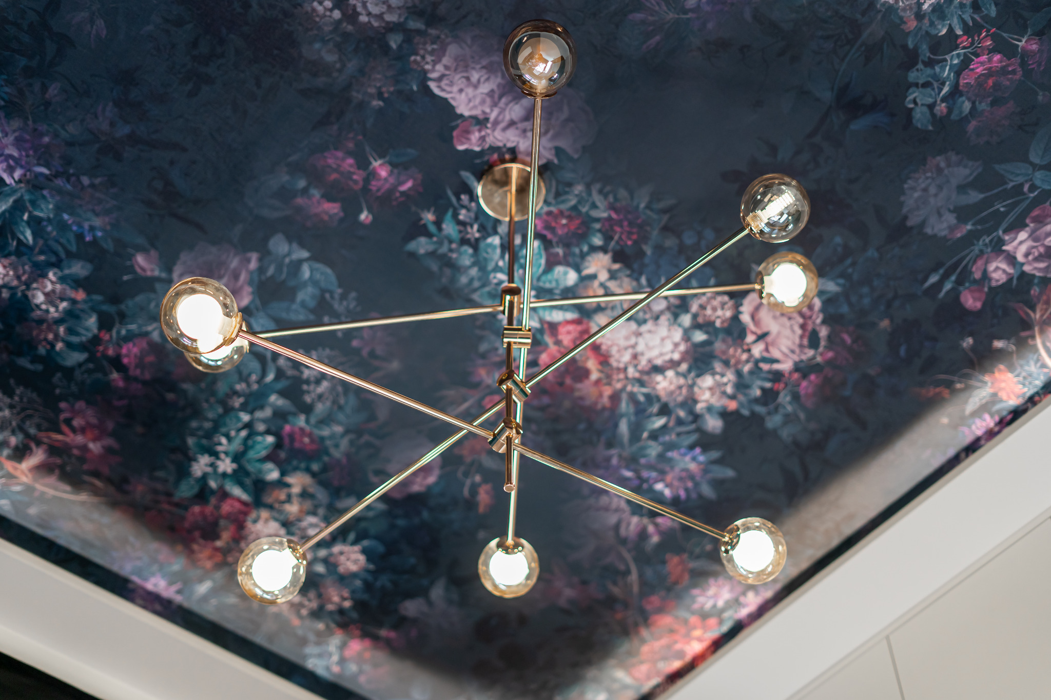 Żyrandol z żarówkami na tle sufitu z ciemną tapetą w kwiaty. Nietypowe oświetlenie wnętrza, widok z dołu.