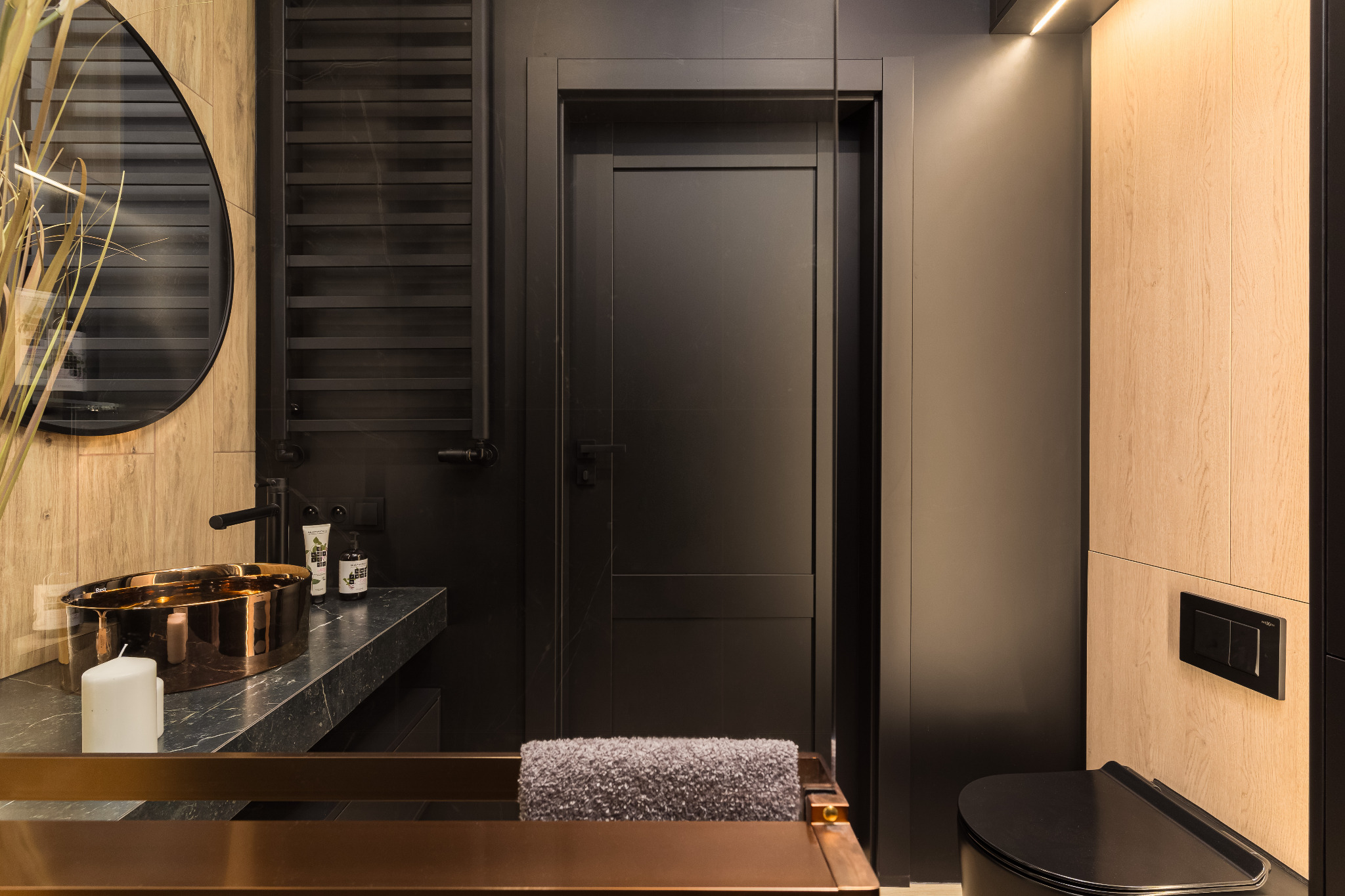 Nowoczesna łazienka w odcieniach czerni i drewna: miedziana umywalka, czarna armatura, drzwi i toaleta. Minimalistyczny design z akcentami naturalnego drewna.