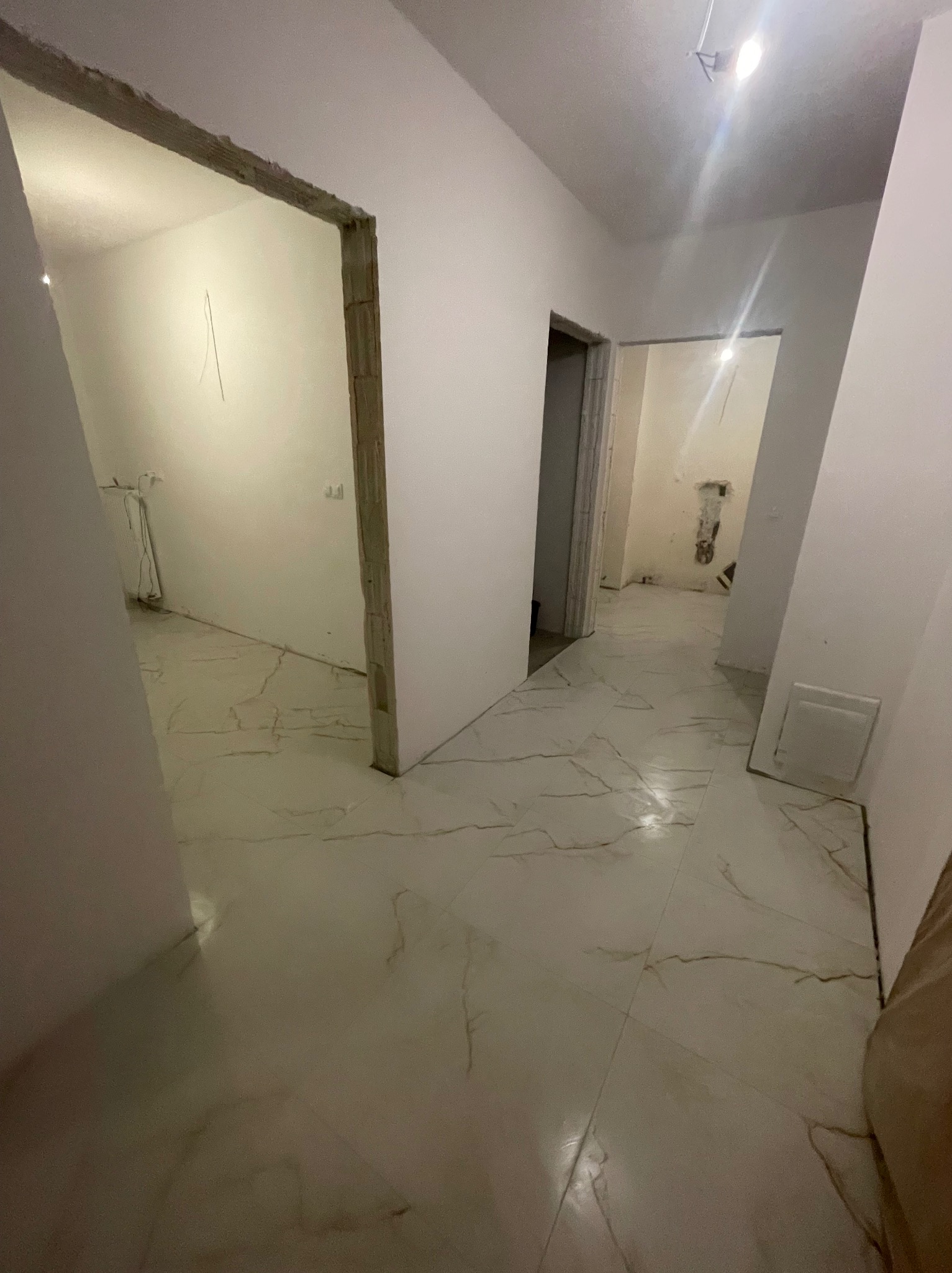 Wykończone wnętrze mieszkania z marmurową podłogą i świeżo pomalowanymi ścianami. Widoczne przejścia do kolejnych pomieszczeń w trakcie remontu.