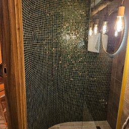 EXACT HOME FIRMA REMONTOWO BUDOWLANA DAWID LISOWSKI - Nowoczesna kabina prysznicowa z mozaiką w odcieniach zieleni, okrągłym lustrem z podświetleniem LED i deszczownicą. Widoczny fragment drewnianej ramy drzwi.