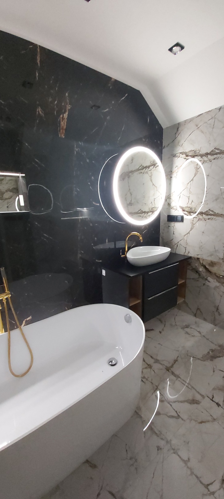 Nowoczesna łazienka z wolnostojącą wanną, marmurowymi płytkami i podświetlanym lustrem. Złota armatura dodaje elegancji. Minimalistyczny design.