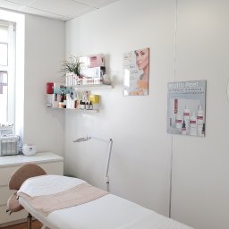 Harmonia Urody - Jasne wnętrze gabinetu kosmetycznego z leżanką, sprzętem i kosmetykami na półkach. Minimalistyczny wystrój, naturalne światło z okna.