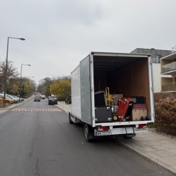 MalardPrzeprowadzki - Ciężarówka z otwartymi drzwiami załadowana bagażami i kartonami na ulicy miejskiej, sugerująca przeprowadzkę. Widoczny numer rejestracyjny pojazdu.