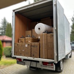 MalardPrzeprowadzki - Ciężarówka wypełniona kartonami i folią bąbelkową, gotowa do transportu. Widoczny numer rejestracyjny i logo Sprinter. Detal: koła z rolkami pod kartonami.