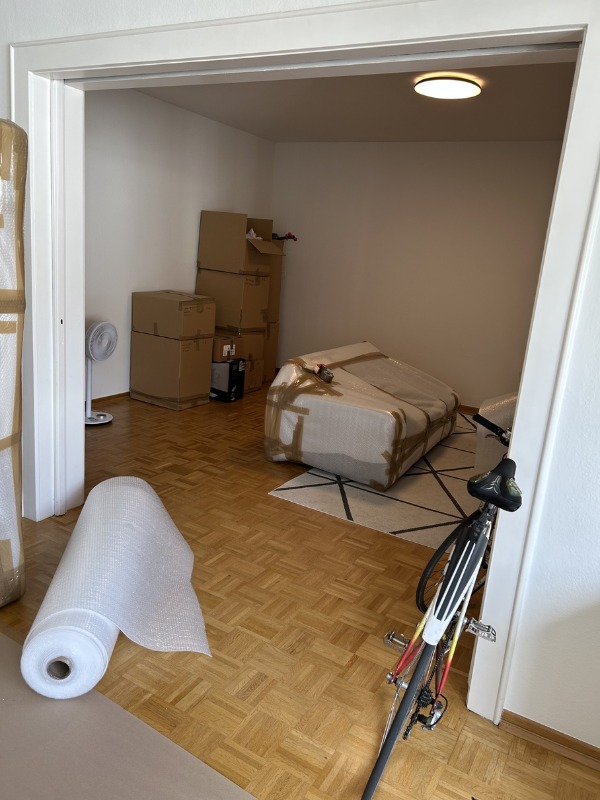 Pokój przed przeprowadzką: kartony, zabezpieczone meble, rower oparty o ścianę, folia bąbelkowa na parkiecie. Widok z perspektywy wejścia do pomieszczenia.