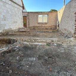BUD-KOP Adam Świerczewski - Przygotowanie terenu pod budowę: wykopane fundamenty, widoczne ściany z cegły i bloczków, błękitne niebo w tle. Etap prac ziemnych przed wylaniem fundamentów.