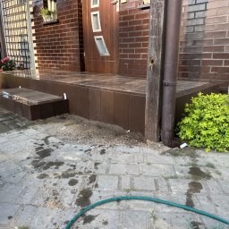 BUD-KOP Adam Świerczewski - Murowany, brązowy ganek z płytkami przed wejściem do domu w Łomży. Widoczny fragment elewacji z cegły i drewniane drzwi z przeszkleniami.