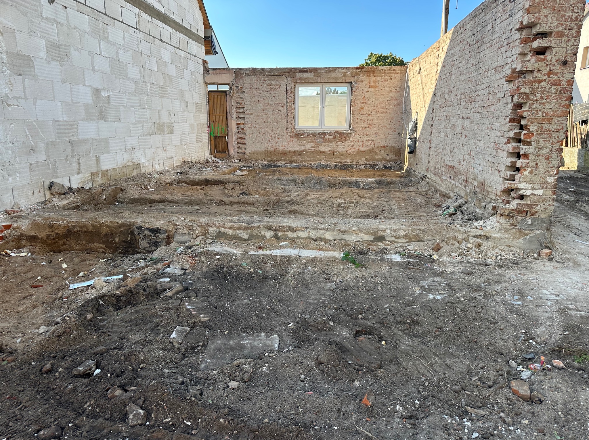 Przygotowanie terenu pod budowę: wykopane fundamenty, widoczne ściany z cegły i bloczków, błękitne niebo w tle. Etap prac ziemnych przed wylaniem fundamentów.