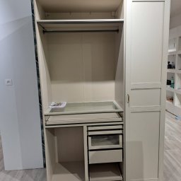 SQUAD S.C. JACEK BARTKOWIAK I KAROL KŁOSEK - Beżowa szafa wnękowa z szufladami i półkami, częściowo zamontowana, widoczne elementy wykończeniowe na suficie. Ujęcie z bliska, prezentujące detale konstrukcji.