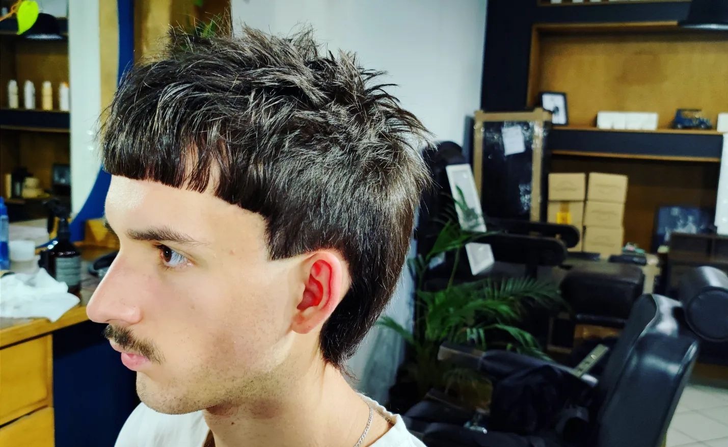 Mężczyzna z awangardową fryzurą: krótka grzywka i dłuższe włosy z tyłu głowy. Widok z profilu, ukazujący precyzyjne cięcie i kształt.