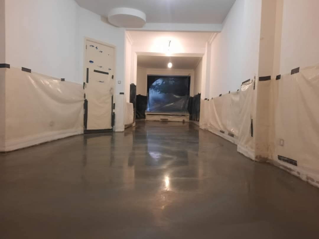 Świeżo wylana, gładka posadzka w pomieszczeniu zabezpieczonym folią malarską. Widoczne odbicia światła na powierzchni. Praca w trakcie realizacji.